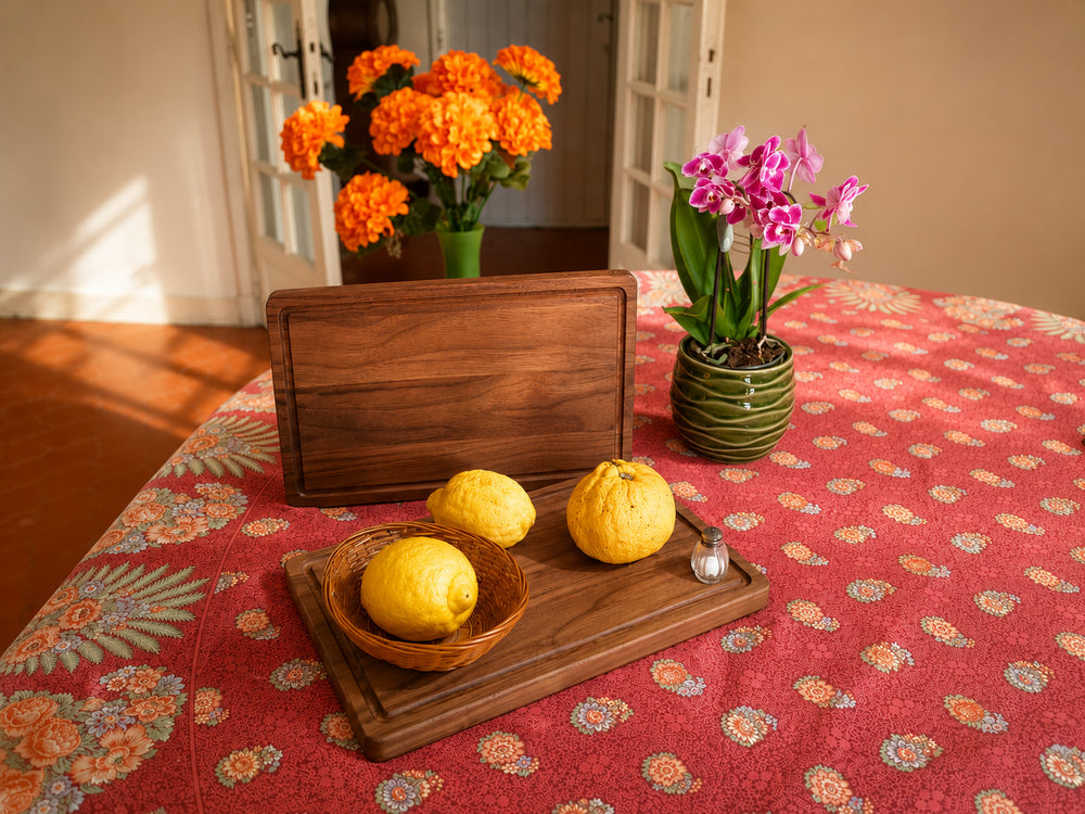 Planche à découper en noyer américain Le Beau Marius sur une table avec des fruits et des fleurs